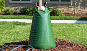 Treegator® Original Single Bag filled next to water hose on mulch close-up cropped